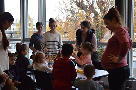 Stand der Mütter- und Väterberatung mit Kindern und Erwachsenen um den Tisch